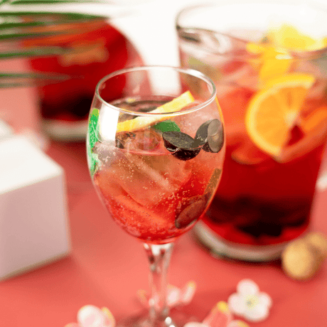 Cóctel Fruit Rosé con frutas frescas, uvas y rodajas de naranja, servido con hielo en copa de vino. Refrescante y elegante.