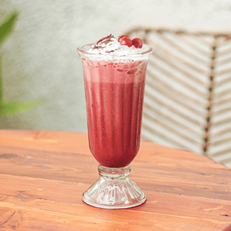 Red Velvet Cherry Frappé en copa vintage con crema batida y cerezas, bebida helada y cremosa ideal para cafés, postres o cocteles irresistibles.