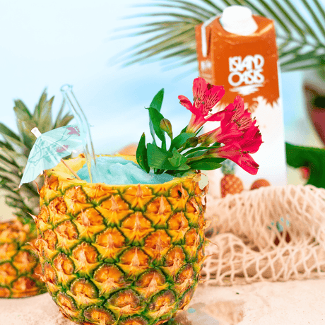 Cóctel Blue Colada tropical servido en piña natural, decorado con flores exóticas y sombrilla, ideal para bebidas veraniegas.