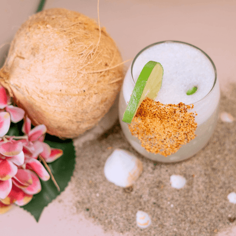 Coctel cremoso de coco con escarchado de chile, decorado con lima fresca y coco natural, ideal para bebidas tropicales refrescantes.